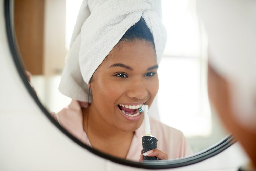 woman getting ready in the mirror brushing her teeth good oral hygiene routine dentist in Timonium Maryland